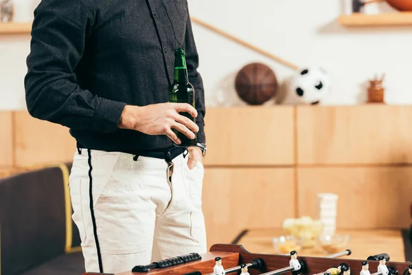 Vista parcial del hombre con botella de cerveza de pie en la cafetería con futbolín - foto de stock