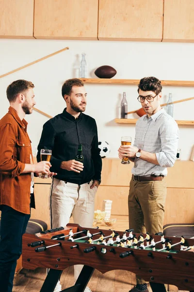 Men with beer in hands talking while resting in cafe with table soccer — Stock Photo