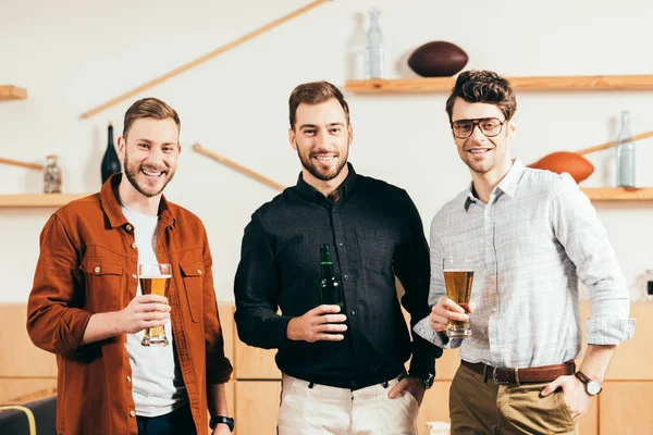 Retrato de hombres sonrientes con cerveza en las manos mirando a la cámara en la cafetería - foto de stock