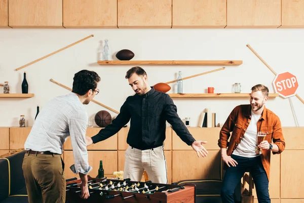 Homem olhando para jovens amigos jogando futebol de mesa no café — Fotografia de Stock