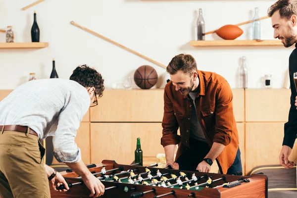 Hombre mirando a jóvenes amigos jugando futbolín en la cafetería - foto de stock