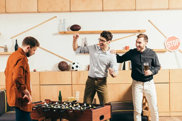 Jóvenes jugando futbolín juntos en la cafetería - foto de stock