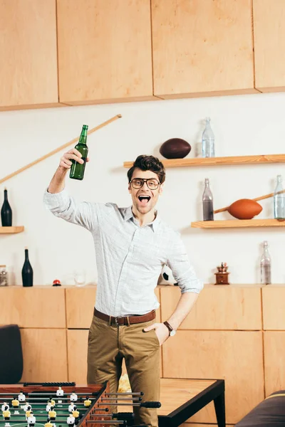 Portrait of happy man in eyeglasses with bottle of beer in hand in cafe — Stock Photo