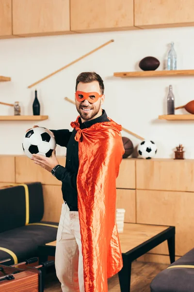 Young smiling man in red superhero costume with soccer ball in cafe — Stock Photo