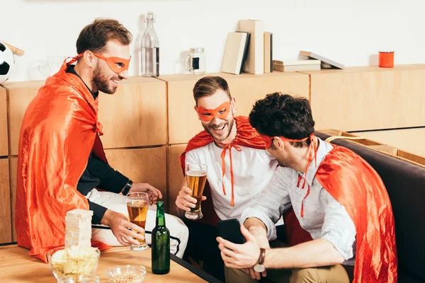 Smiling friends in superhero costumes spending time together in cafe — Stock Photo