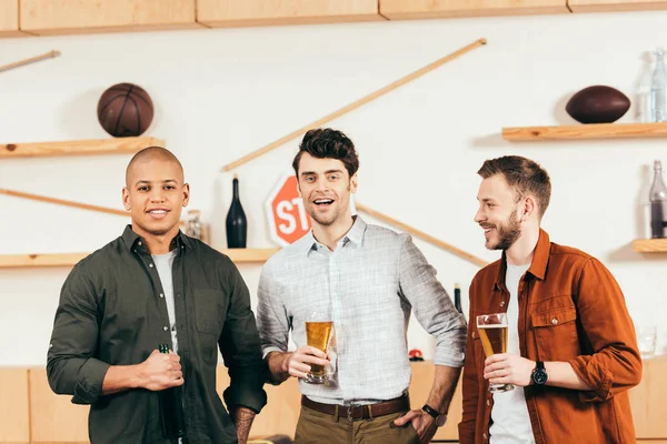 Portrait of cheerful multiracial friends with beer looking at camera in cafe — Stock Photo