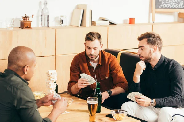 Hombres multiculturales jugando a las cartas mientras pasan tiempo juntos en la cafetería - foto de stock