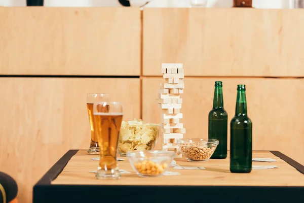 Vista de cerca de la cerveza, aperitivos y bloques juego de madera en la mesa en la cafetería - foto de stock