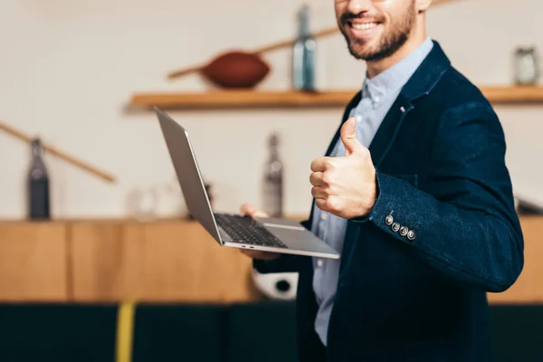 Tiro recortado de homem de negócios sorridente com laptop mostrando polegar no café — Fotografia de Stock