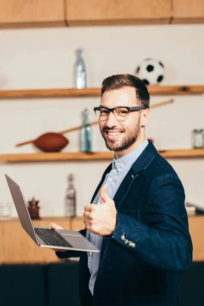 Vue latérale de souriant homme d'affaires avec ordinateur portable montrant pouce vers le haut dans le café — Photo de stock