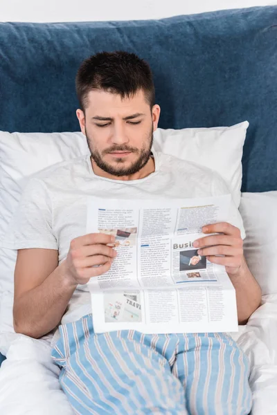 Schöner Mann im Pyjama, der morgens zu Hause im Bett Zeitung liest — Stockfoto