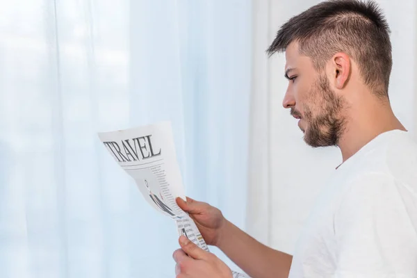 Homem bonito lendo jornal de viagem na cama de manhã em casa — Fotografia de Stock