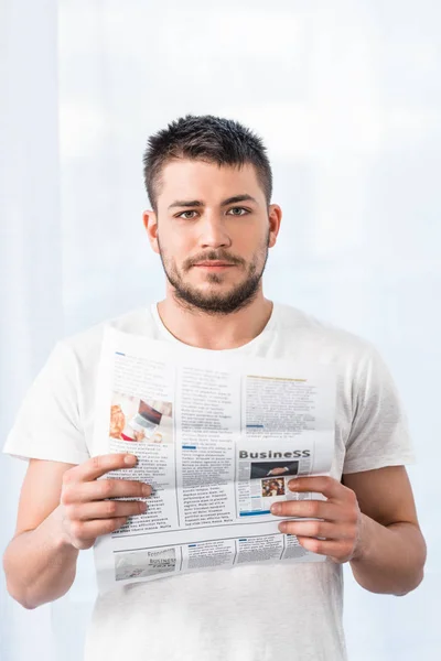Homem bonito segurando jornal e olhando para a câmera de manhã em casa — Fotografia de Stock