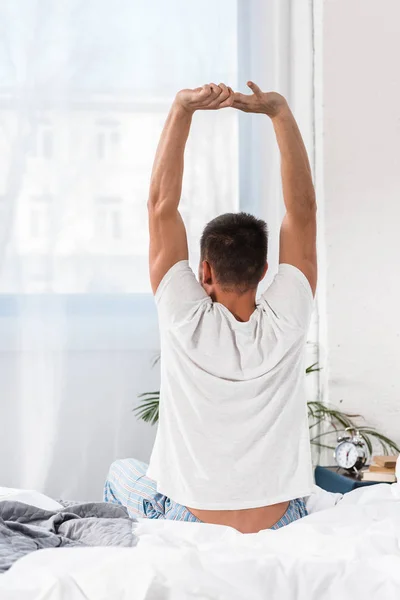 Rückansicht eines Mannes, der sich morgens im Schlafzimmer dehnt — Stockfoto