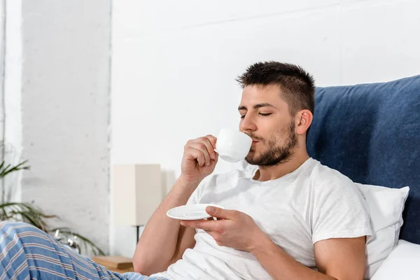 Hombre guapo bebiendo café en la mañana en el dormitorio - foto de stock