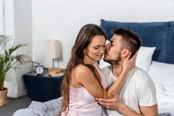 Namorado de pijama abraçando e beijando namorada na cama no quarto — Fotografia de Stock