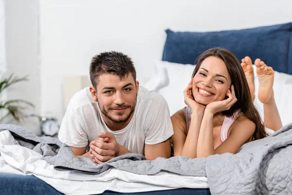 Sorrindo namorada e namorado de pijama deitado na cama no quarto e olhando para a câmera — Fotografia de Stock