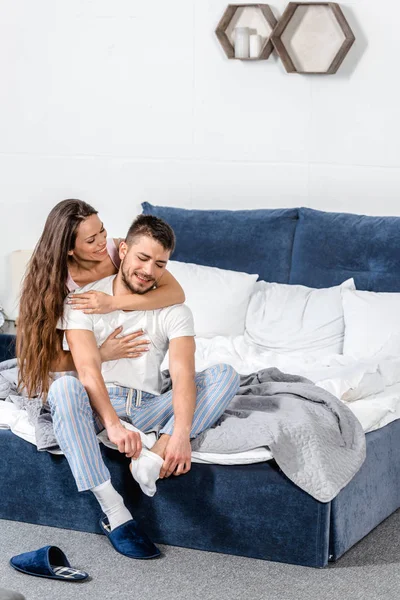 Girlfriend hugging boyfriend and he wearing socks on bed in bedroom — Stock Photo
