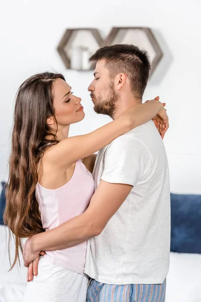 Couple in pajamas hugging and going to kiss in bedroom — Stock Photo