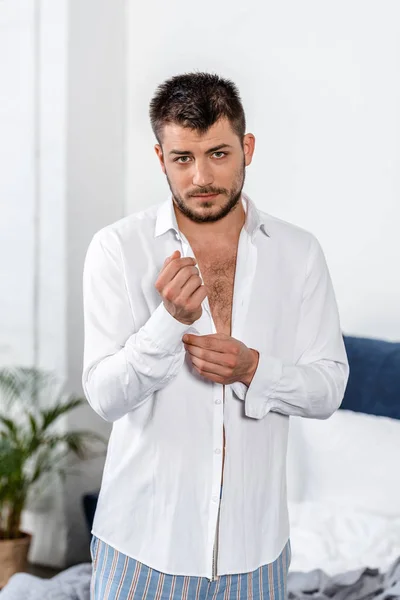 Handsome man buttoning cuff in weekday morning in bedroom and looking at camera — Stock Photo