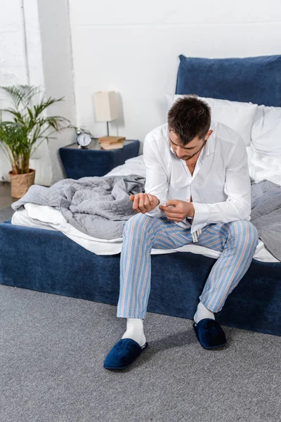 Homem bonito sentado na cama e abotoando manguito na manhã de dia da semana no quarto — Fotografia de Stock