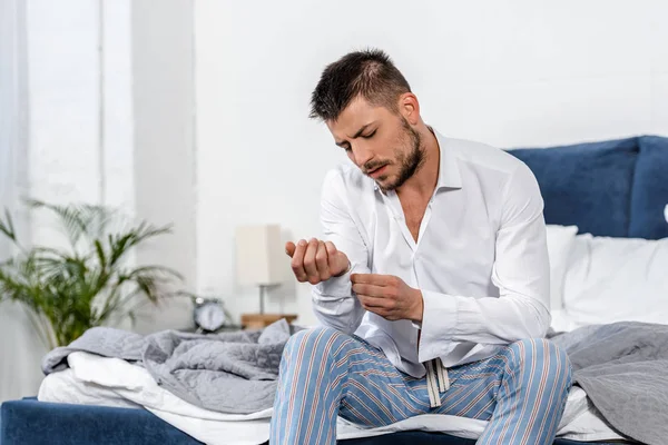 Handsome man sitting on bed and buttoning cuff in weekday morning in bedroom — Stock Photo