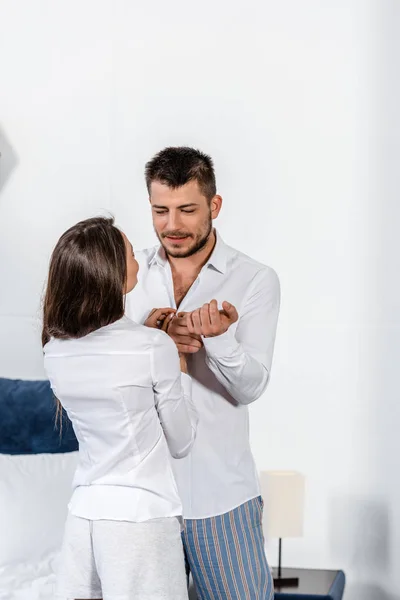 Handsome boyfriend buttoning cuff and girlfriend buttoning his shirt in weekday morning in bedroom — Stock Photo