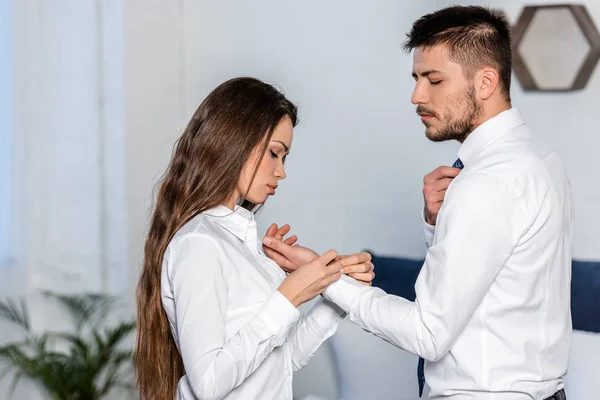 Vista lateral de novia abotonamiento novio manguito en la mañana en casa, concepto de sexismo - foto de stock