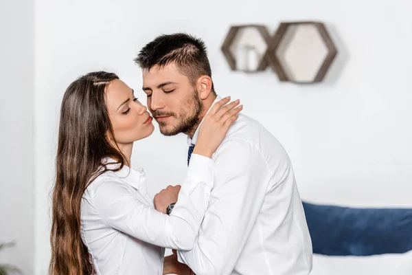 Vista lateral de novia besar novio en la mañana en el dormitorio antes del trabajo - foto de stock