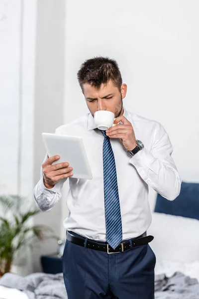 Homem bonito bebendo café e usando tablet de manhã no quarto — Fotografia de Stock