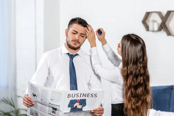 Girlfriend styling boyfriend hair and he reading business newspaper at home, social role concept — Stock Photo