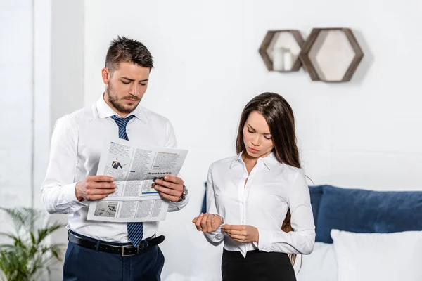 Girlfriend buttoning cuff and boyfriend reading business newspaper at home, gender equality concept — Stock Photo