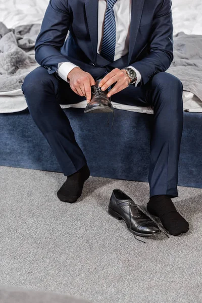 Cropped image of man in suit wearing shoes and sitting on bed in morning in bedroom — Stock Photo