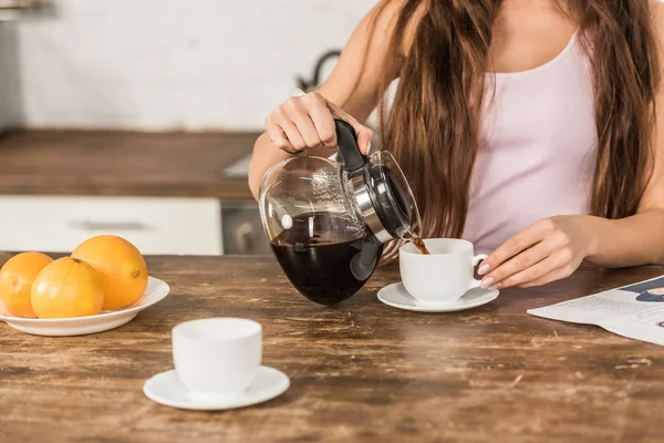 Imagen recortada de la mujer vertiendo café en la taza por la mañana en la cocina - foto de stock