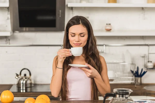Красива жінка з закритими очима нюхає ароматну каву вранці на кухні — стокове фото