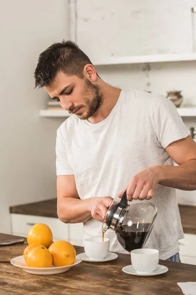 Handsome man pouring coffee into cup in morning at kitchen — Stock Photo