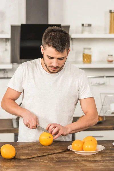 Schöner Mann schneidet morgens in der Küche Orangen — Stockfoto