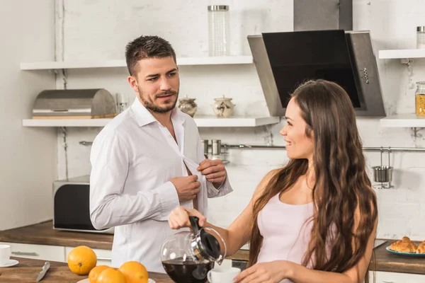 Freund knöpft Hemd und Freundin gießt zu Hause Kaffee in Tasse, Konzept der Ungleichheit — Stockfoto