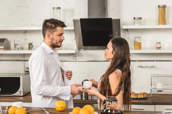 Namorada dando xícara de café para namorado de manhã na cozinha — Fotografia de Stock