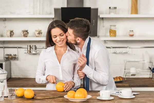 Novio besando novia mientras ella corte naranjas en la mañana en la cocina, concepto de estereotipos de género - foto de stock