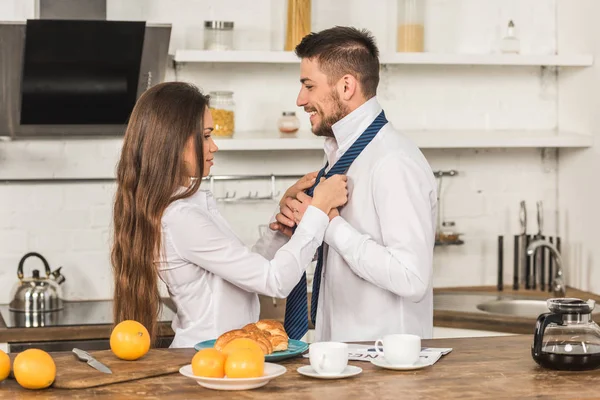 Petite amie attacher petit ami cravate le matin à la cuisine, concept de sexisme — Photo de stock