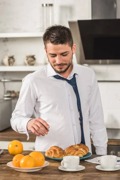 Homem bonito tomando croissant de manhã na cozinha — Fotografia de Stock