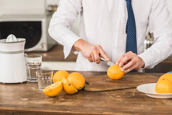 Image recadrée de l'homme coupant des oranges pour le jus le matin à la cuisine — Photo de stock