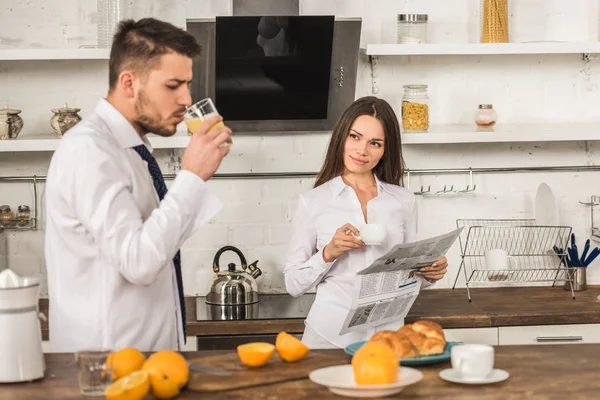 Namorado beber suco e namorada ler jornal na cozinha, conceito de igualdade de gênero — Fotografia de Stock