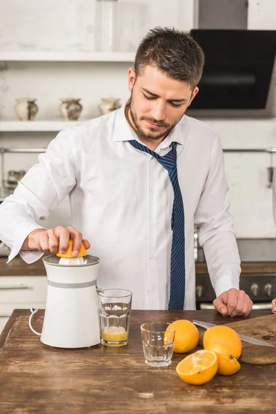 Bell'uomo che fa succo d'arancia con spremiagrumi al mattino in cucina — Foto stock