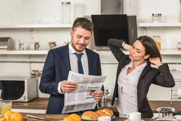 Boyfriend reading newspaper and girlfriend touching hair in kitchen, gender equality concept — Stock Photo