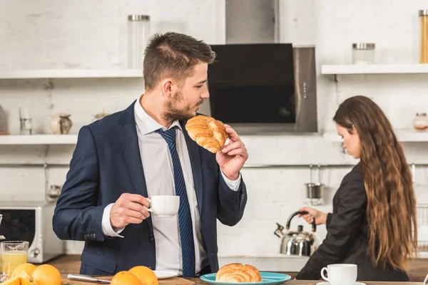 Boyfriend having breakfast and girlfriend putting kettle on stove at home, gender stereotypes concept — Stock Photo