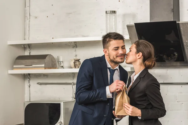 Girlfriend giving lunch to boyfriend and kissing him in morning at kitchen, social roles concept — Stock Photo