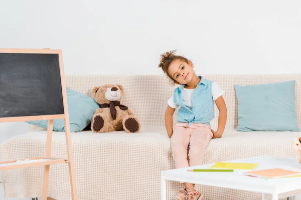 Schöne afrikanisch-amerikanische Kind sitzt auf dem Sofa und lächelt in die Kamera — Stockfoto