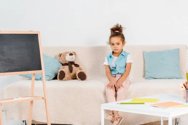 Full length view of adorable african american child sitting on couch and looking at camera — Stock Photo